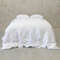White bedding on a bed with pillows against a neutral wall.