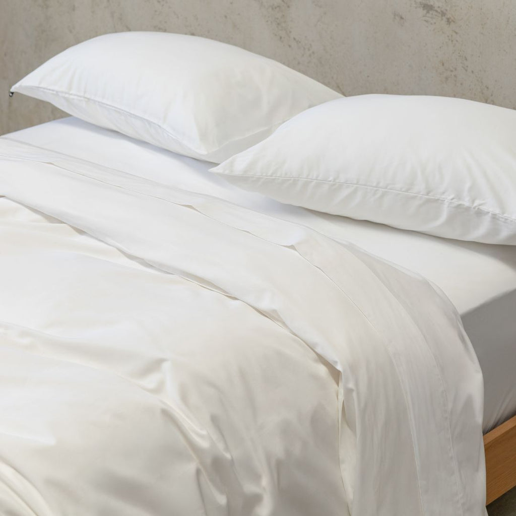 White bedding set with two pillows on a bed against a neutral wall.