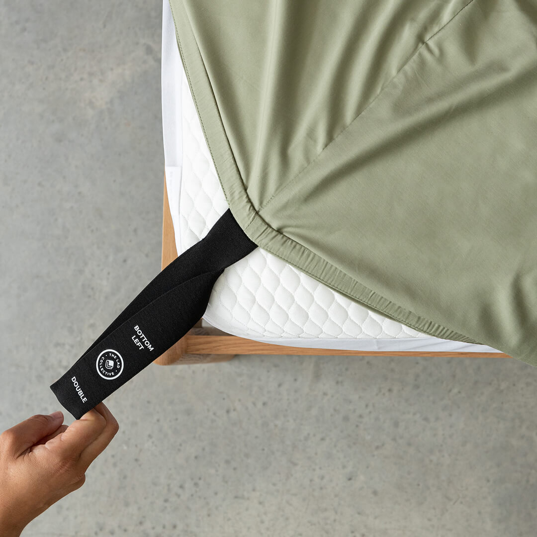 A hand pulling a labelled corner loop on a TLC fitted sheet